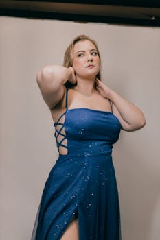 Fashion portrait of a woman in a glamorous blue evening dress, posing indoors.