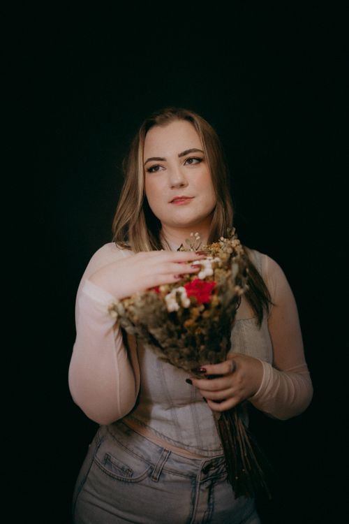 Free Fashion portrait of a woman holding a bouquet against a deep black backdrop. Stock Photo