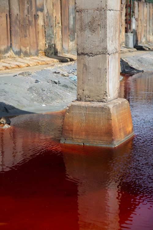 Free Concrete column reflects in contaminated red water, showcasing industrial decay and environmental pollution. Stock Photo