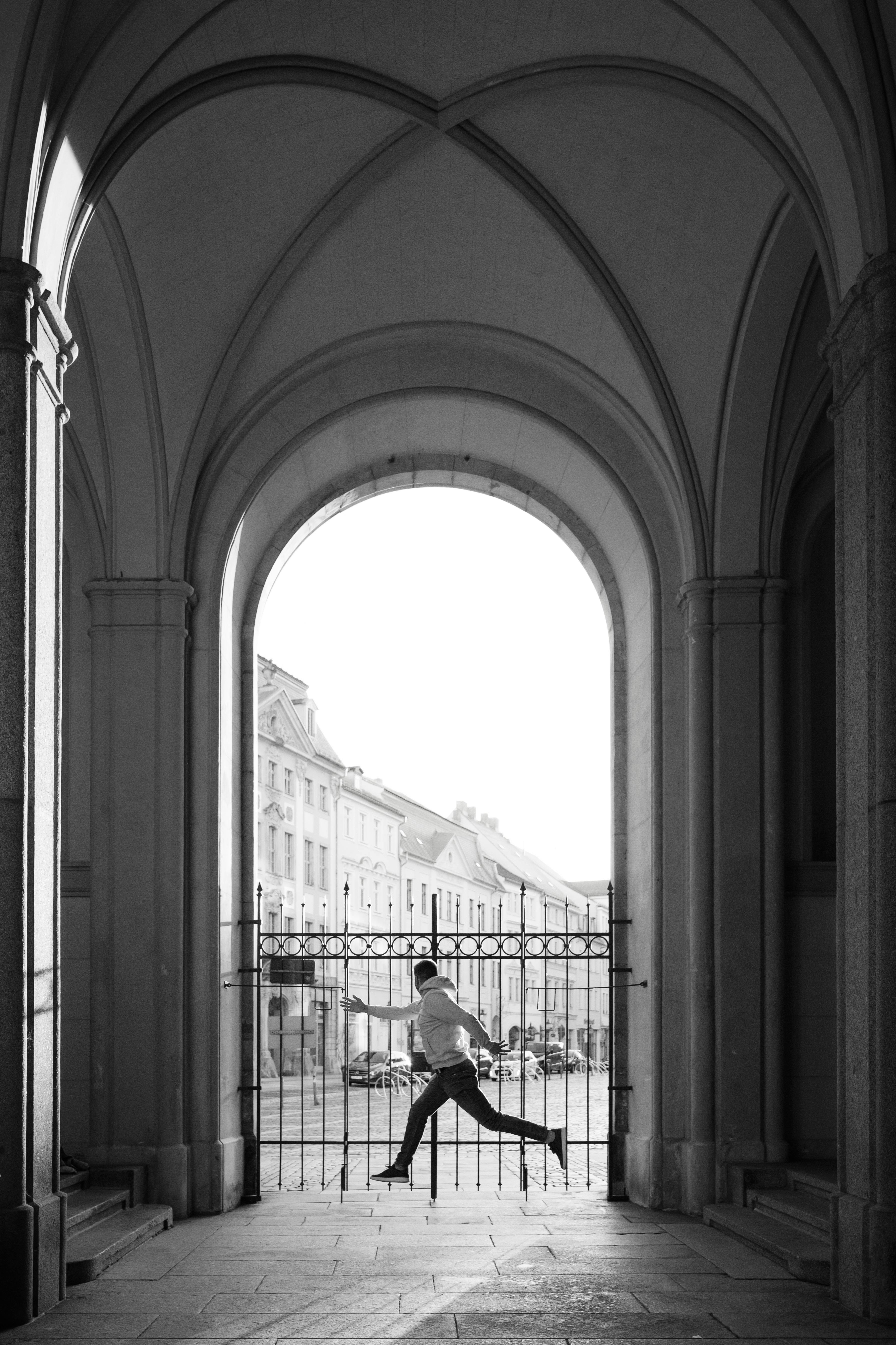 Black and white photo capturing motion of a runner under Zittau's arches in a city setting.