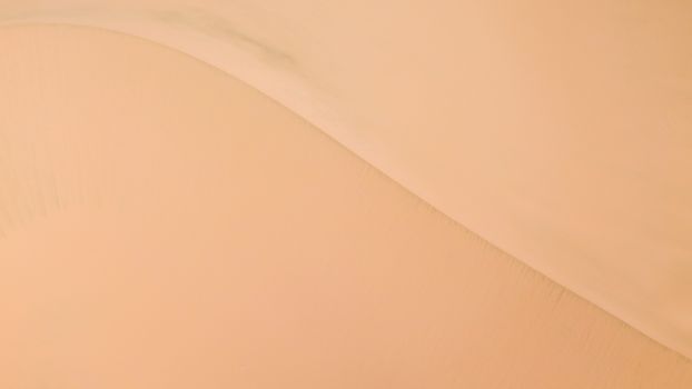 Smooth aerial view of sand dunes creating a tranquil desert landscape.