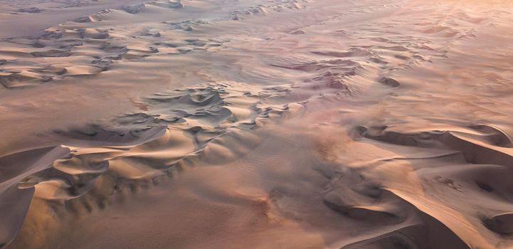 Stunning aerial shot of vast desert sand dunes bathed in warm sunset hues.