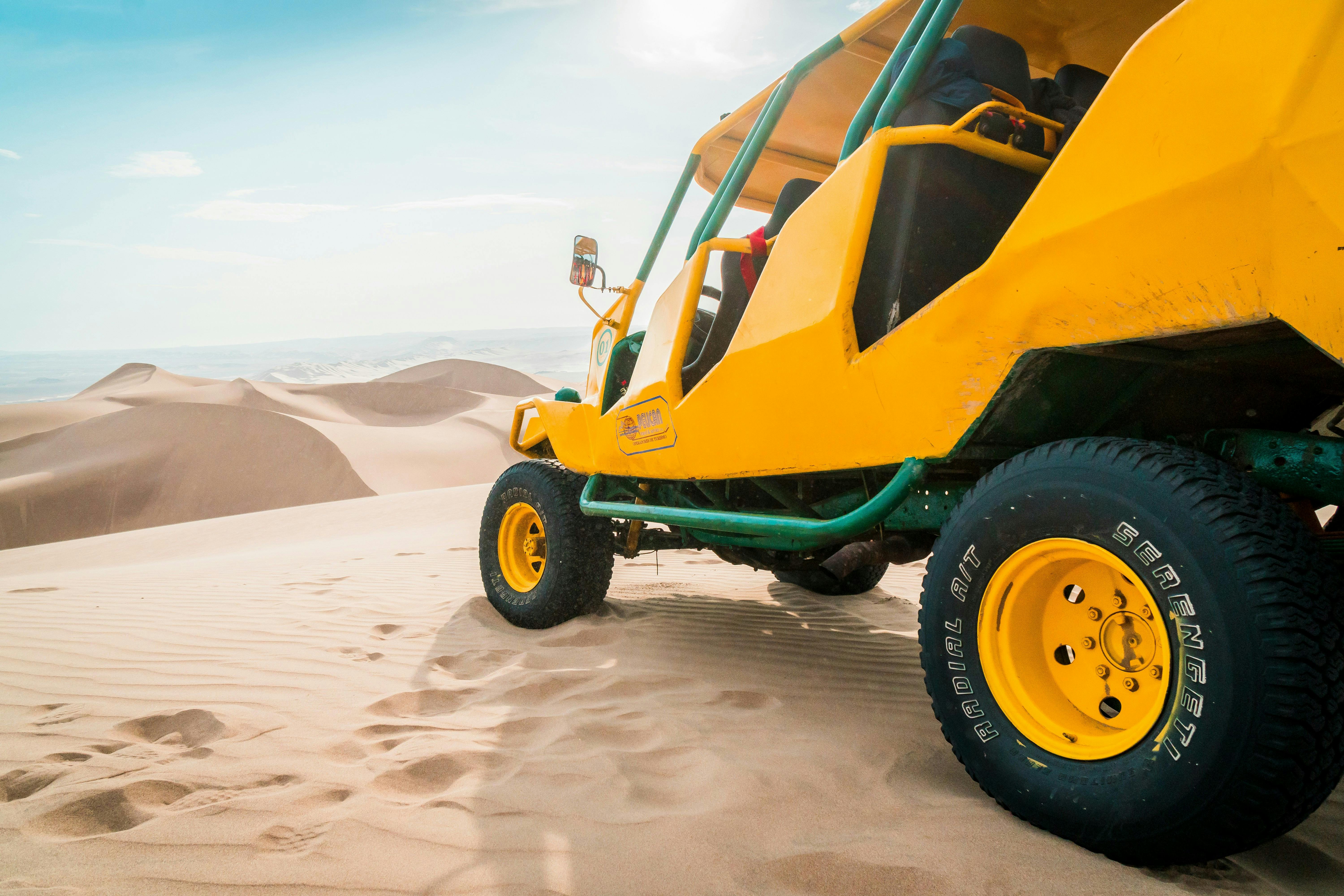A vibrant yellow dune buggy on sandy desert dunes under clear skies.
