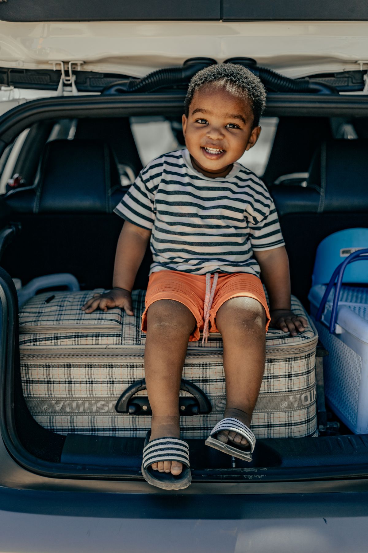 A child sits in the trunk of a car with luggage, a general editorial travel-preparation image