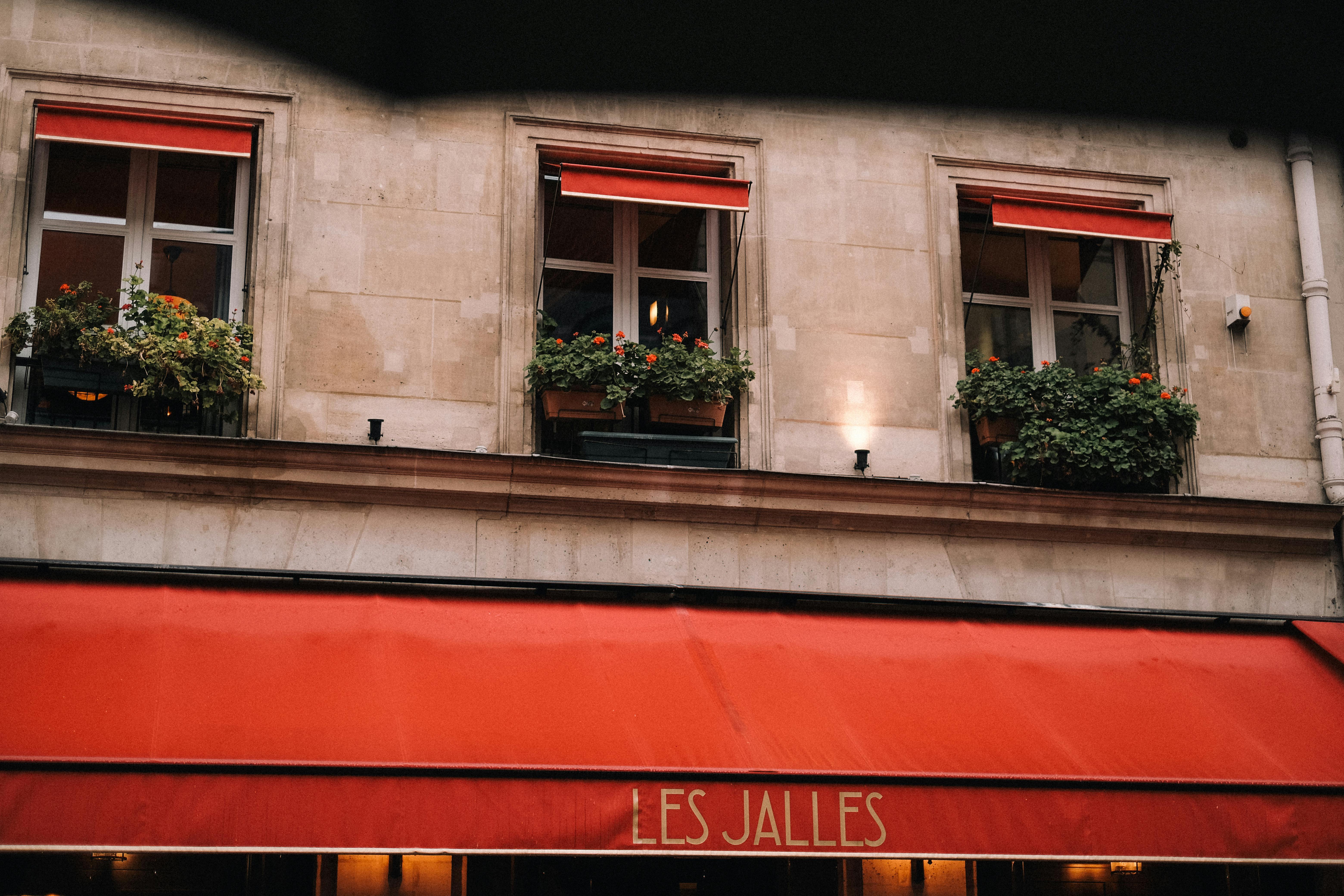 A picturesque Parisian building facade with red awnings and floral window boxes in an urban setting.