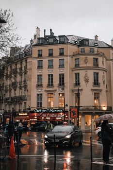 A rainy evening on a bustling Paris street with people, cars, and iconic architecture.