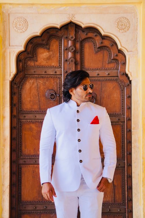 Free Man in a white suit with red pocket square standing in front of an ornate wooden door. Stock Photo
