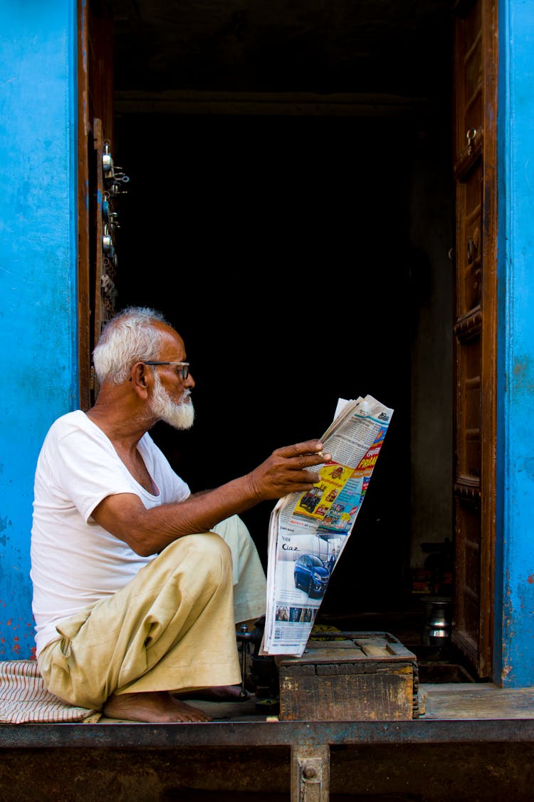 Old Man Sitting While Holding Newspaper Article