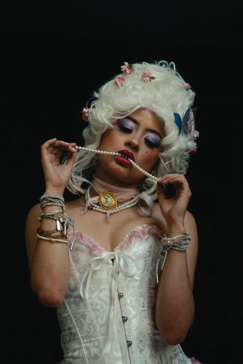 Free A woman in an ornate costume with a corset, wig, and pearls in a studio setting. Stock Photo