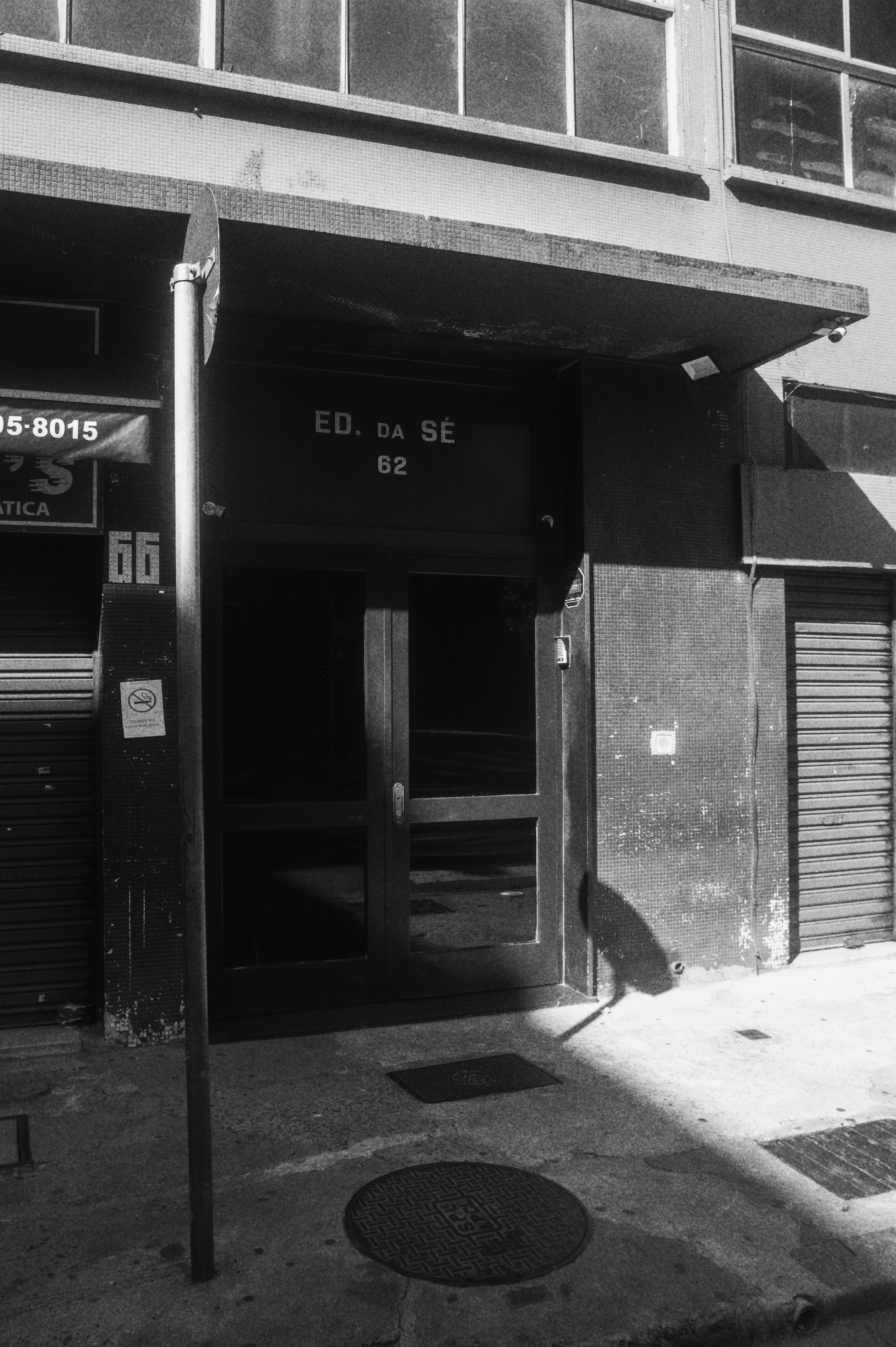 A black and white photo of a city building entrance with visible door and sidewalk.