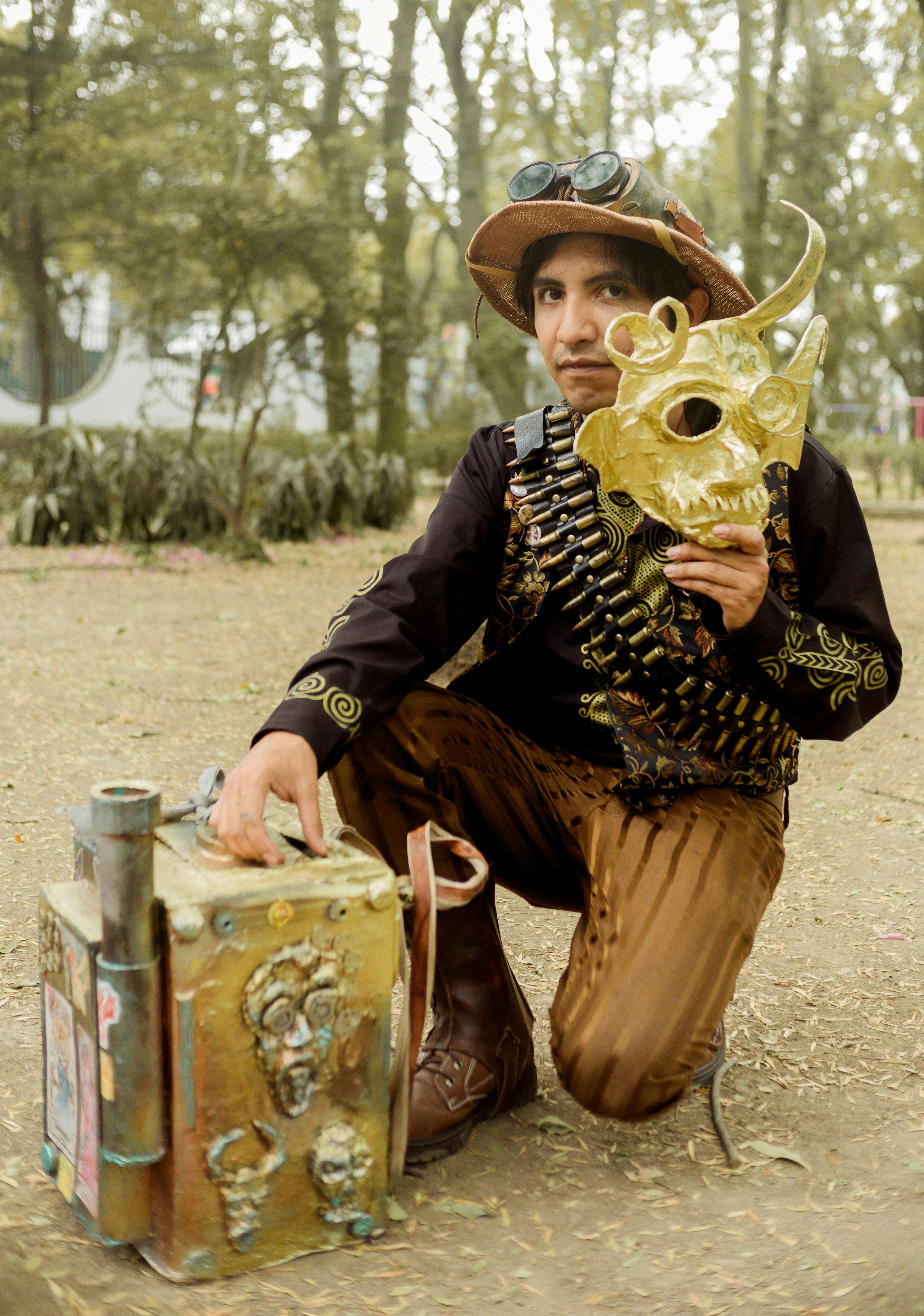 Steampunk enthusiast with gold mask kneels with suitcase in a park, Mexico City.