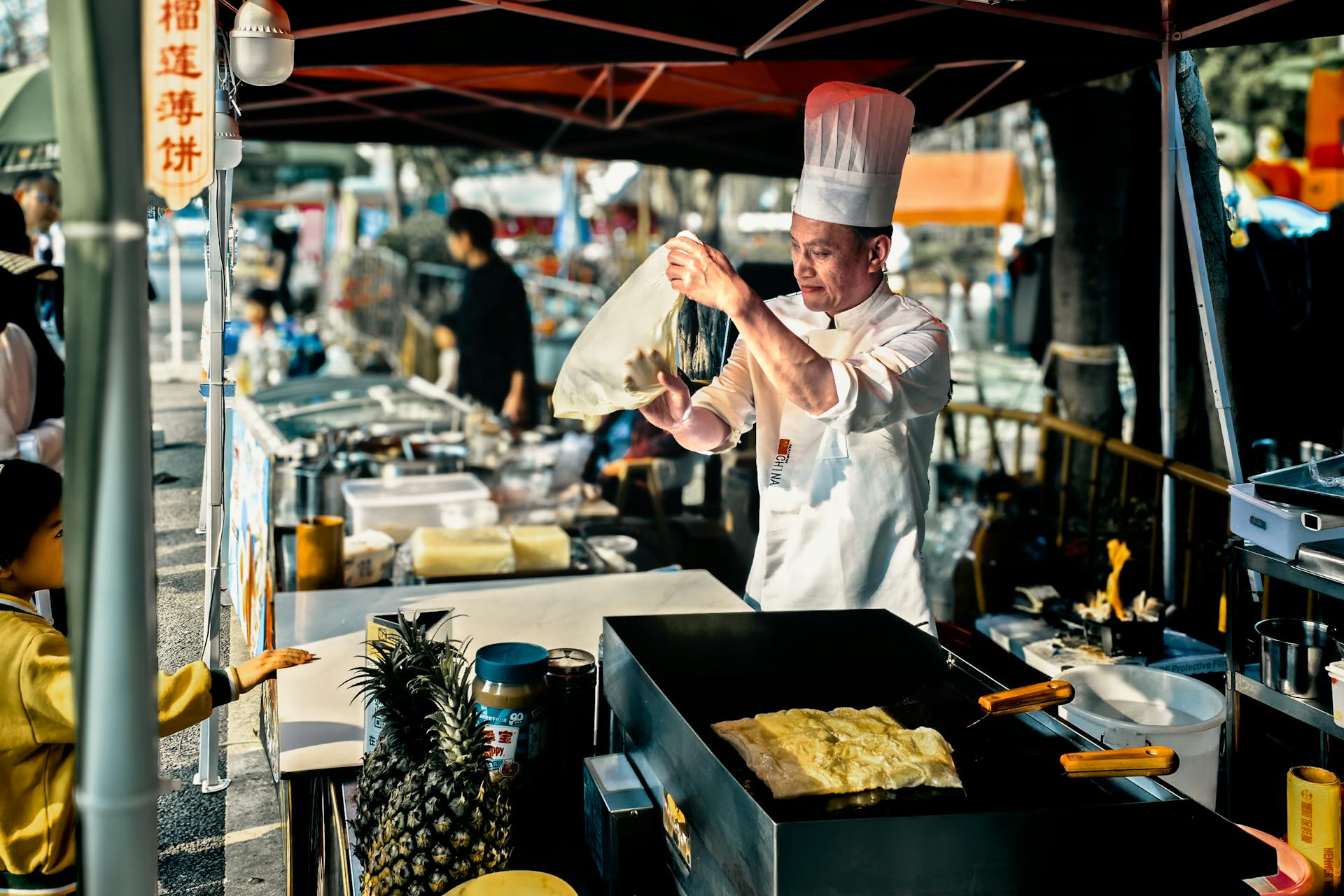 Chef in Shenzhen street market making traditional Chinese crepes at an outdoor stall.