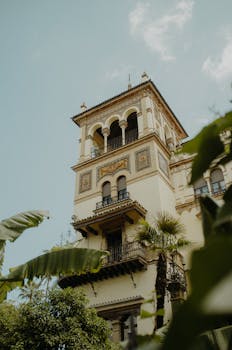 Low angle view of a historic building in Sevilla, Spain, with ornate balconies and tropical plants.