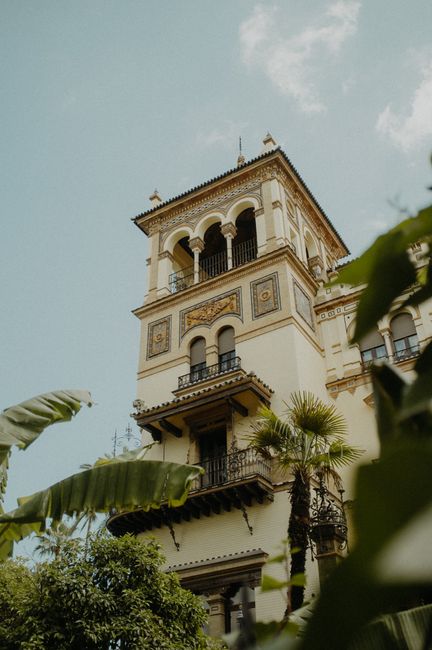 Low angle view of a historic building in Sevilla, Spain, with ornate balconies and tropical plants.