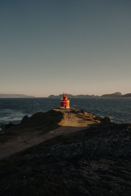 Captivating view of a red lighthouse on the rugged Aldán coastline with a clear sea backdrop.