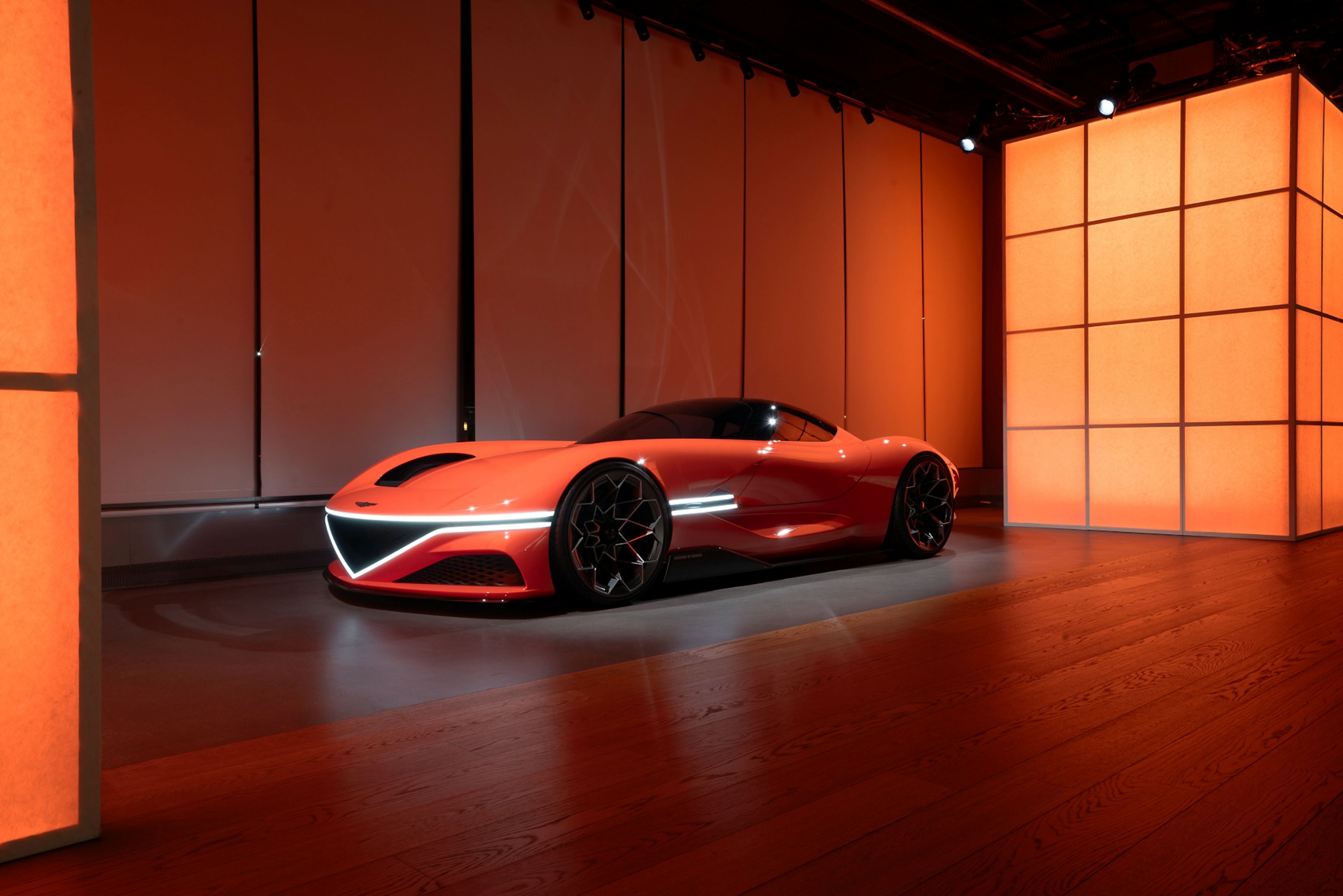 Futuristic red sports car in an indoor studio with vibrant lighting.
