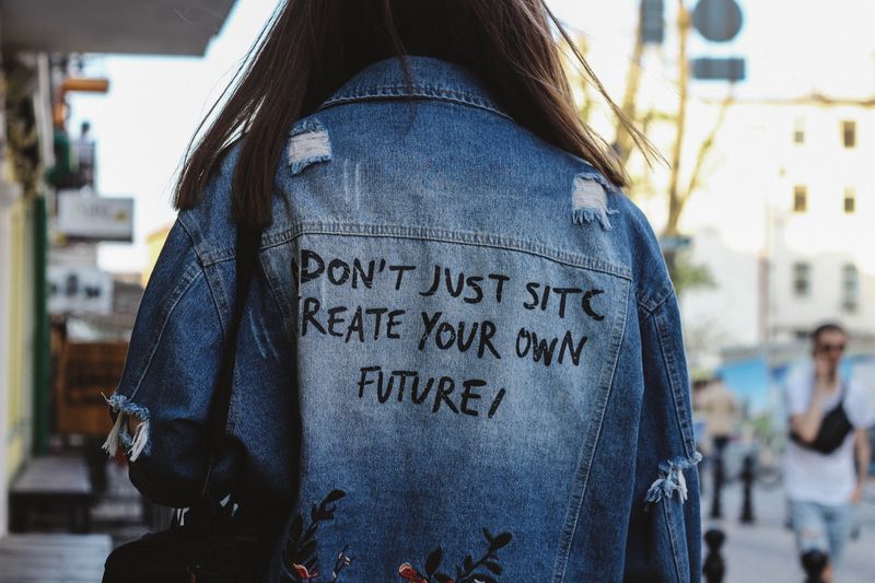 Vista trasera de una mujer en chaqueta vaquera con un mensaje inspirador en una calle urbana.