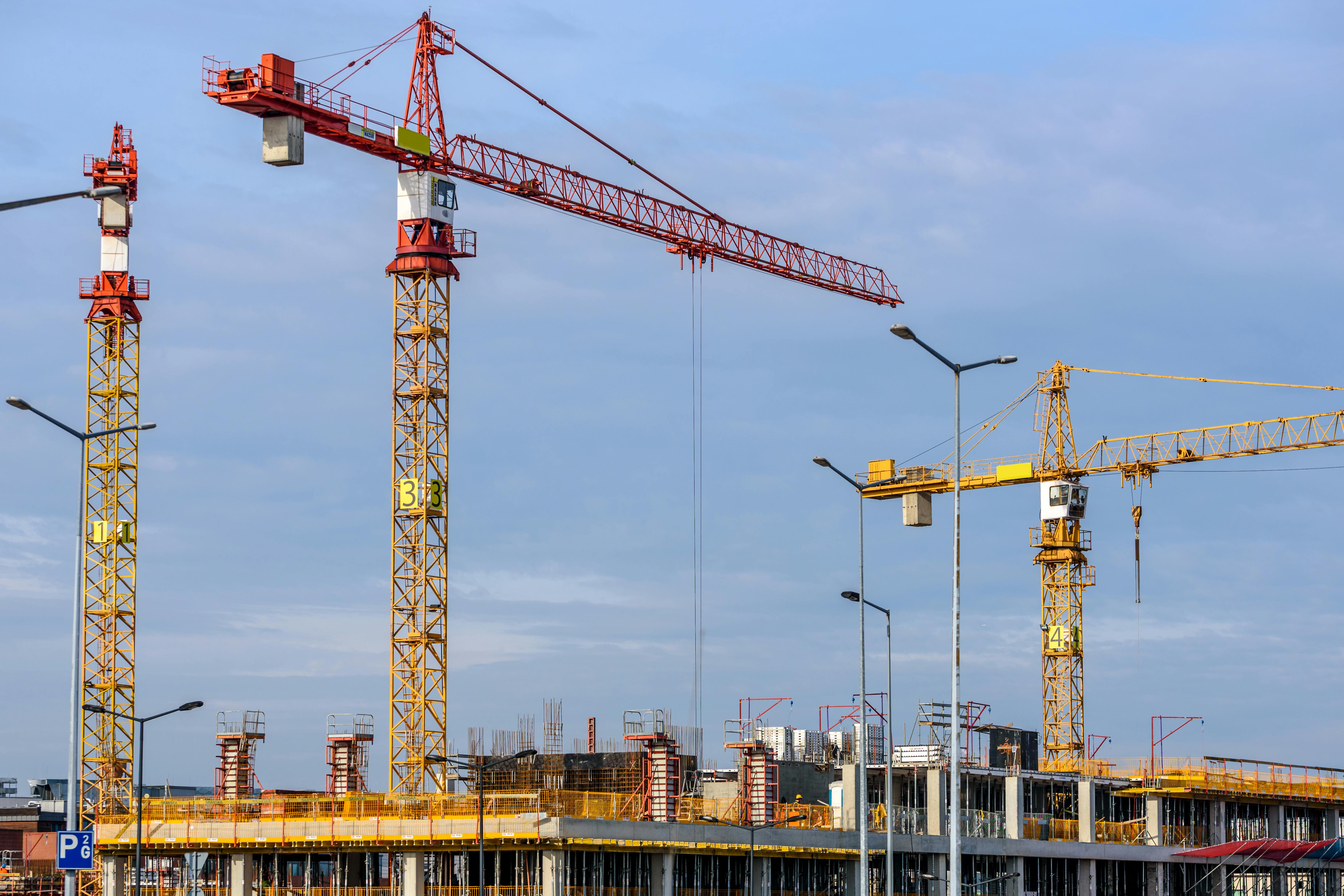 three yellow and red tower cranes under clear blue sky