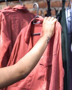 A close-up shot of a hand holding a salmon-colored shirt on a clothing rack.