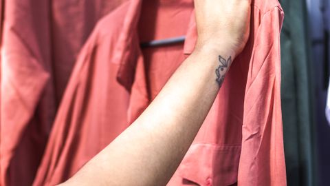 A close-up shot of a hand holding a salmon-colored shirt on a clothing rack.