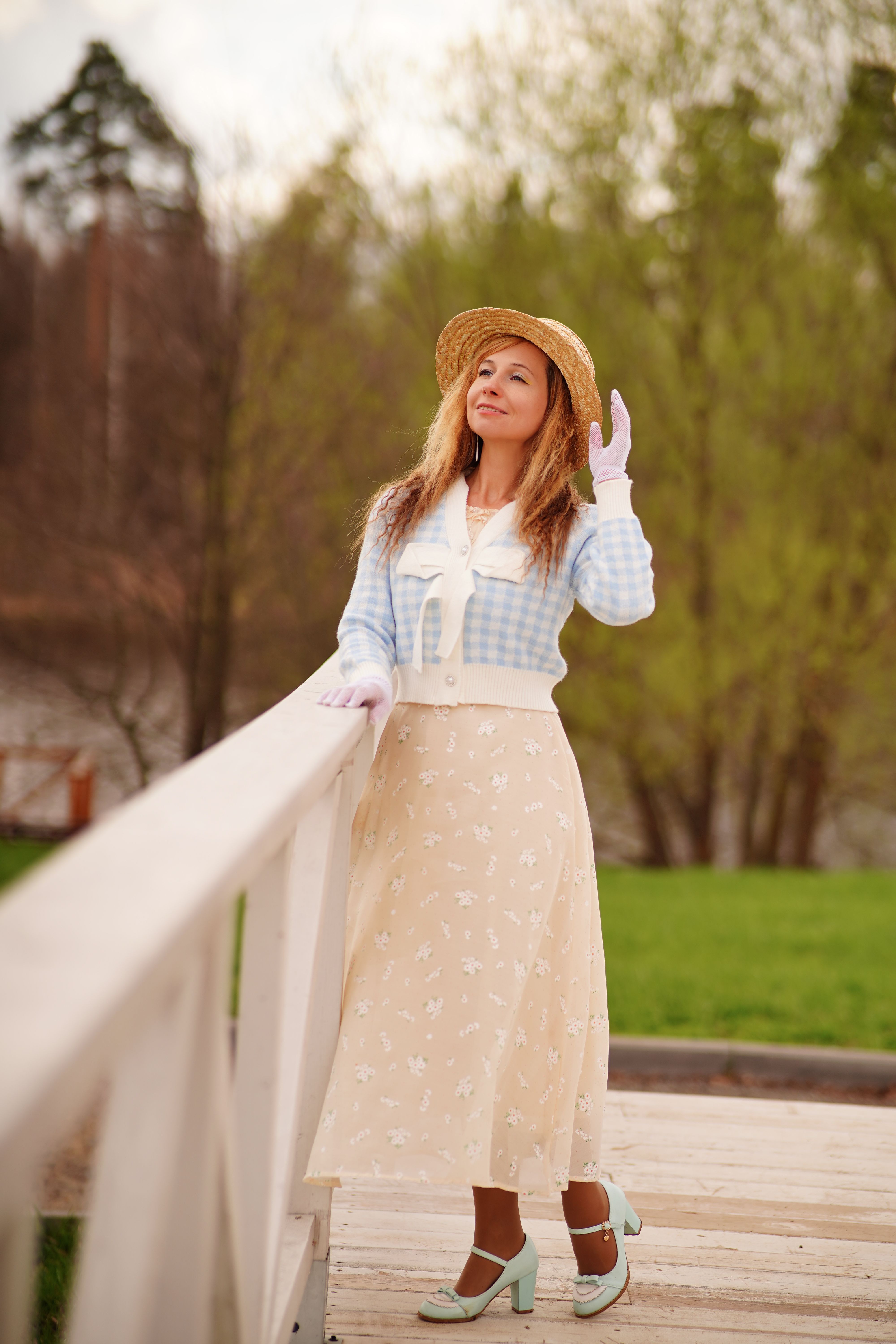 Elegant woman in stylish pastel attire posing on a bridge in a park during fall.
