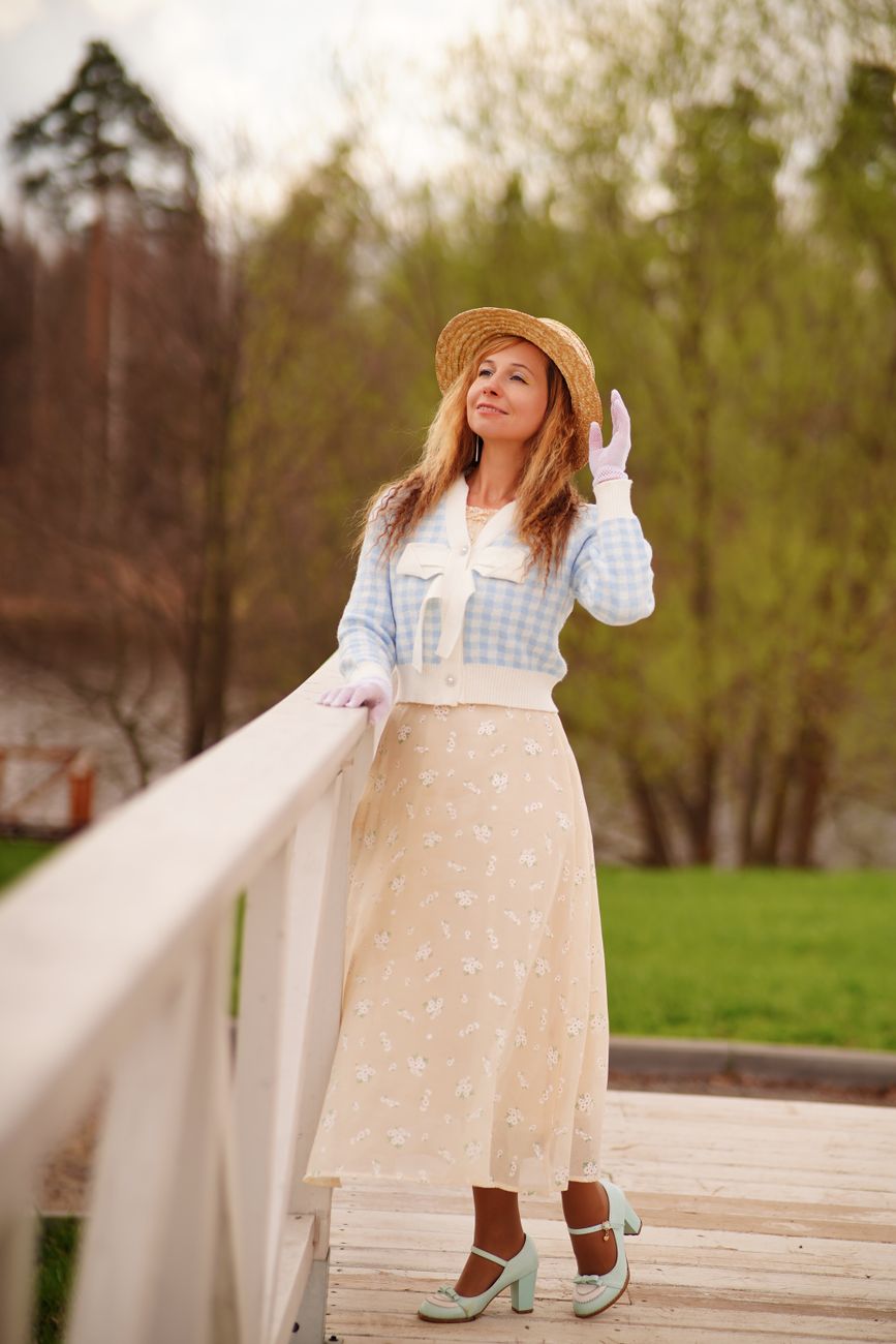 Elegant woman in stylish pastel attire posing on a bridge in a park during fall.