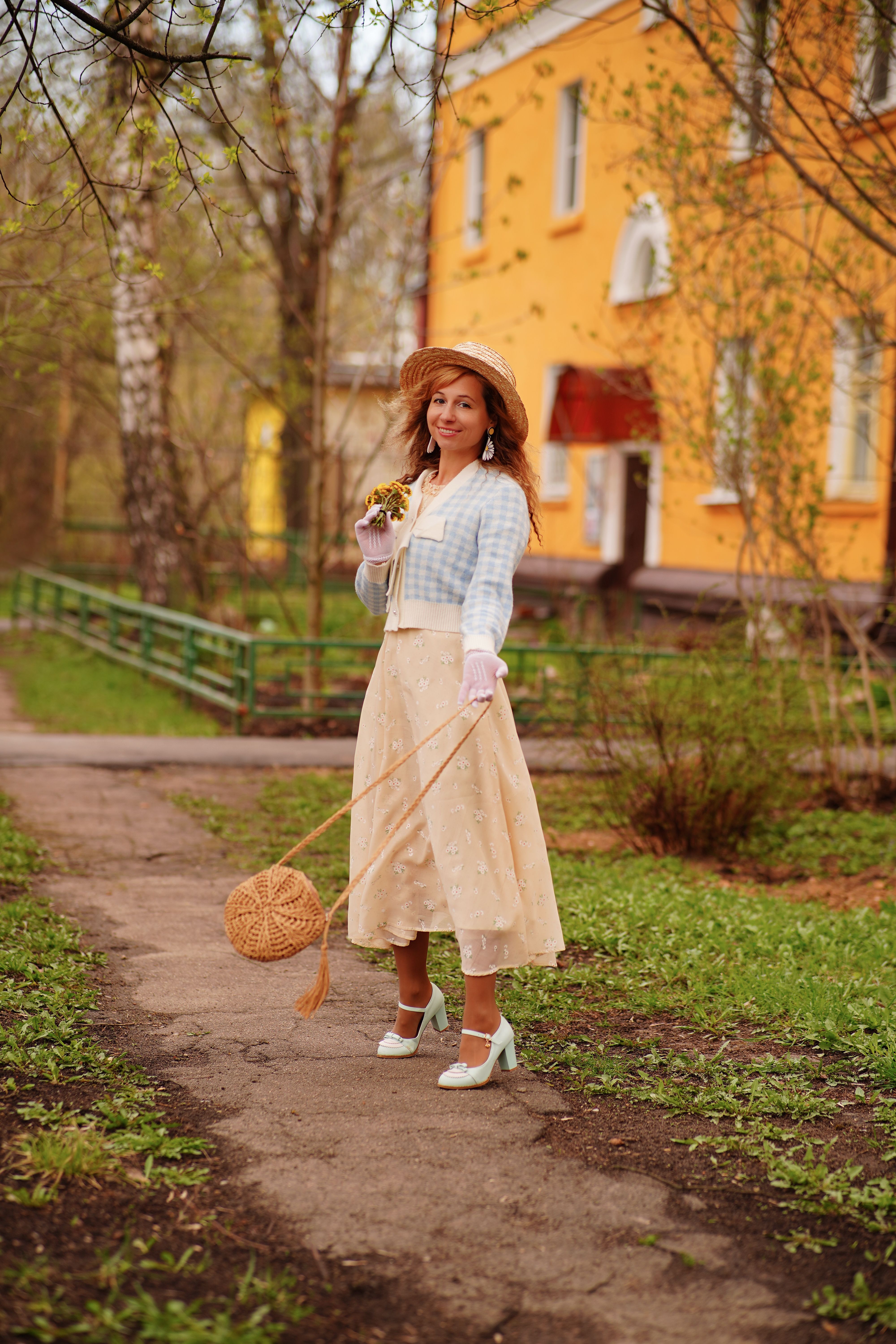 Woman in vintage outfit posing outdoors with a wicker bag and bouquet in Shchyolkovo, Russia.