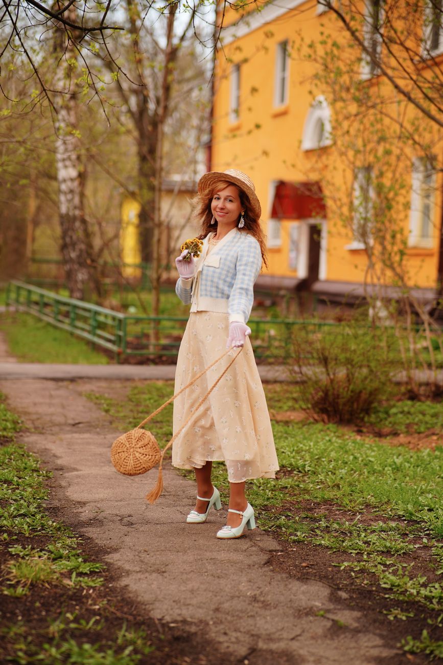 Woman in vintage outfit posing outdoors with a wicker bag and bouquet in Shchyolkovo, Russia.