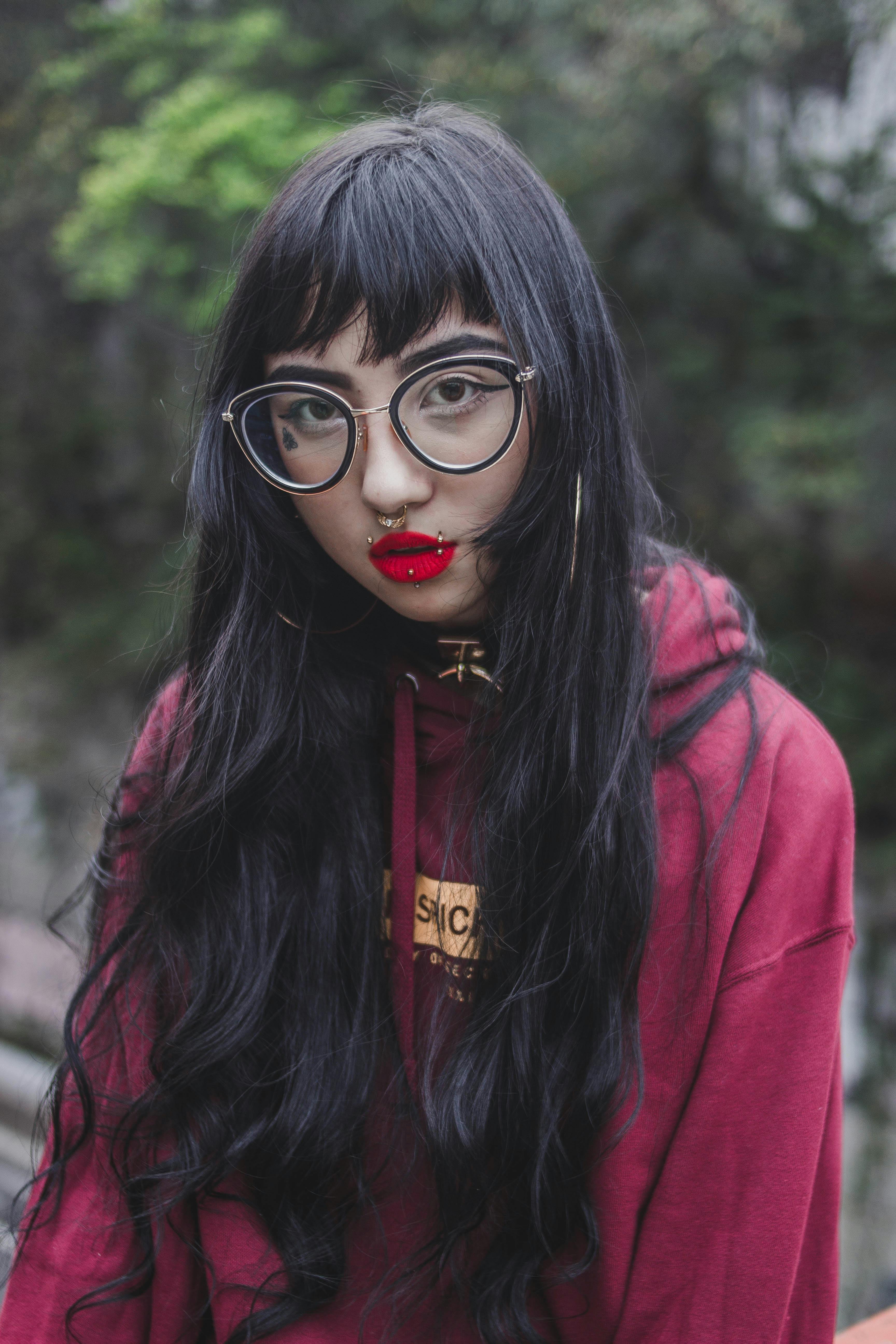 一个戴着眼镜、有穿孔、黑头发的时尚女人穿着红色连帽衫站在户外