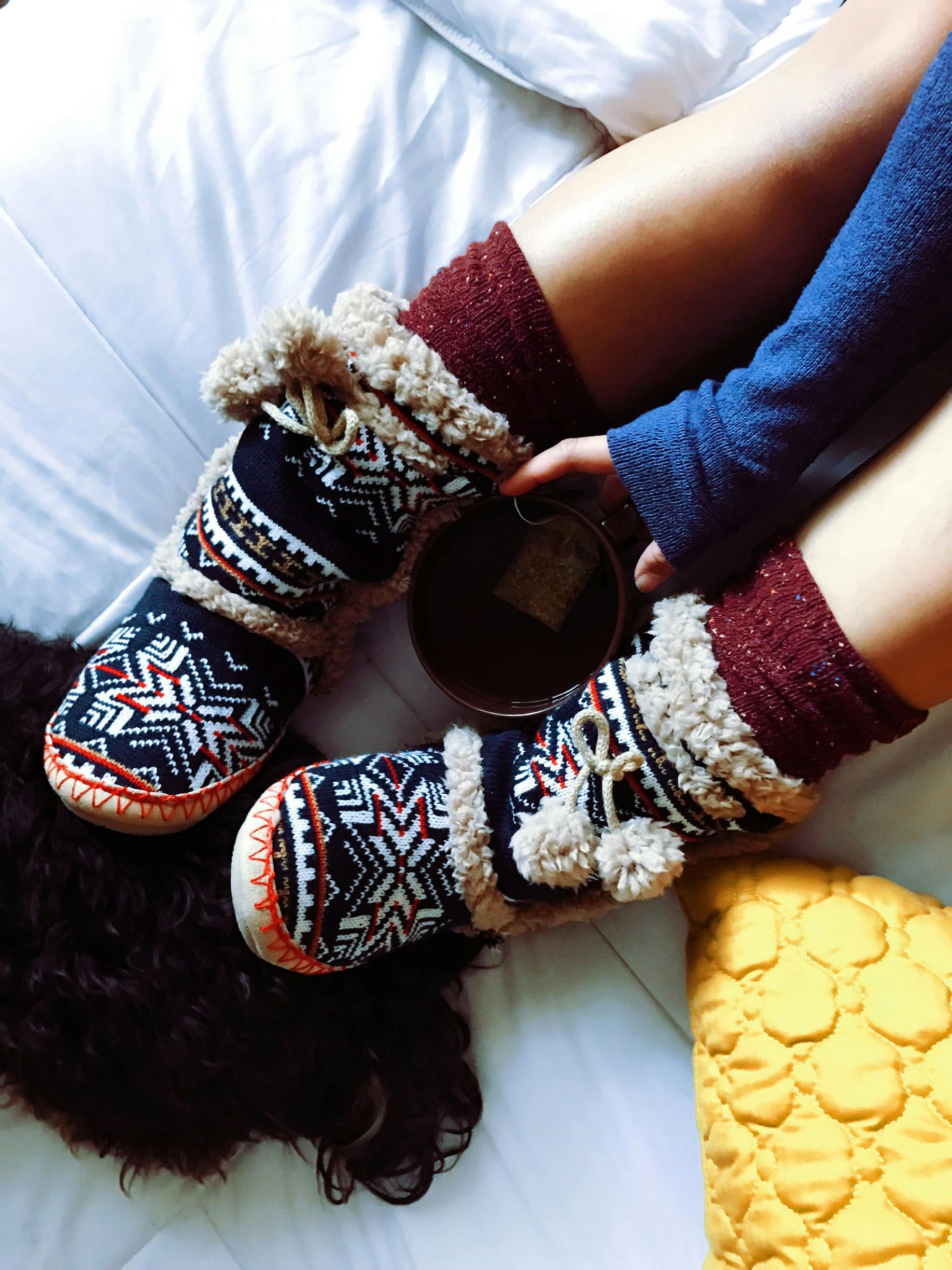 Top view of cozy woolen slippers and a warm drink on a bed, perfect for winter mornings.