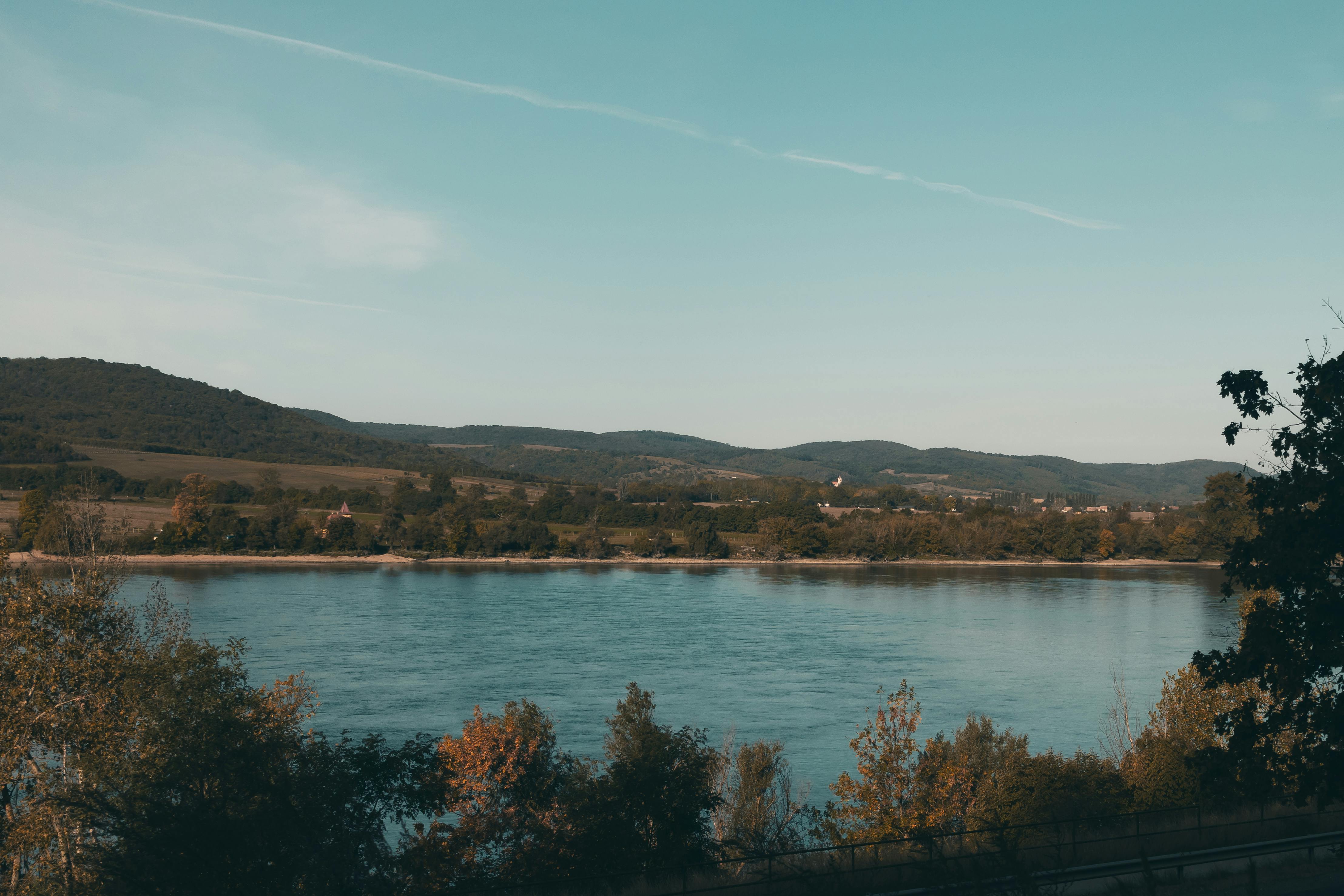 Serene view of a river surrounded by trees and hills in Estergon, Hungary during daytime.