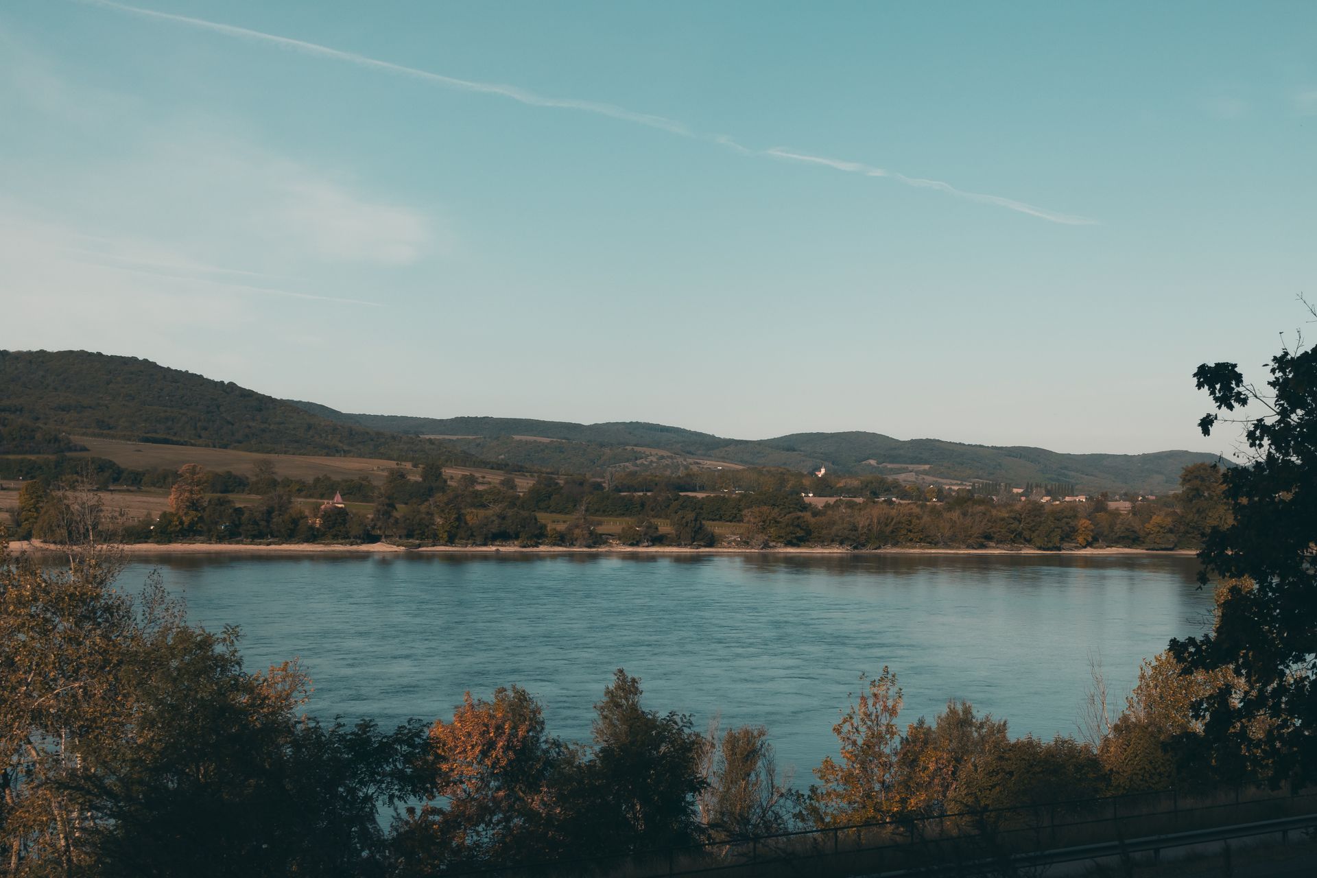 Serene view of a river surrounded by trees and hills in Estergon, Hungary during daytime.