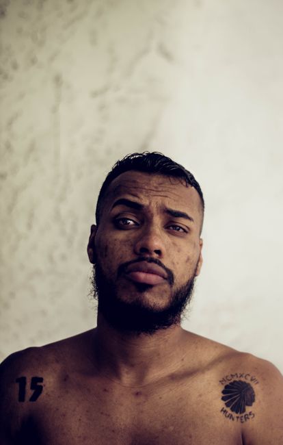 Shirtless man with tattoos and facial hair, gazing thoughtfully.