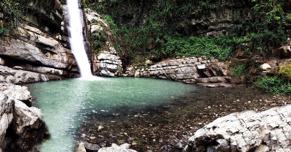 A wide shot of Tagbo Falls plunging into a dark green pool, surrounded by lush tropical vegetation, with no visible tourists