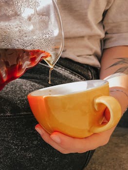 Close-up of a hand pouring fresh coffee into a vibrant yellow mug. Perfect for coffee lovers.