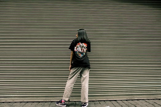 一名女子穿着休闲街头服饰，站在金属百叶窗前