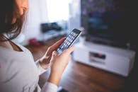 在舒适的家庭环境中，一位女性正在室内浏览智能手机，这突显了现代技术与通信的融合