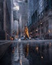 一名身穿黄色外套的男子穿过阴雨的城市街道，建筑高耸，倒影丰富