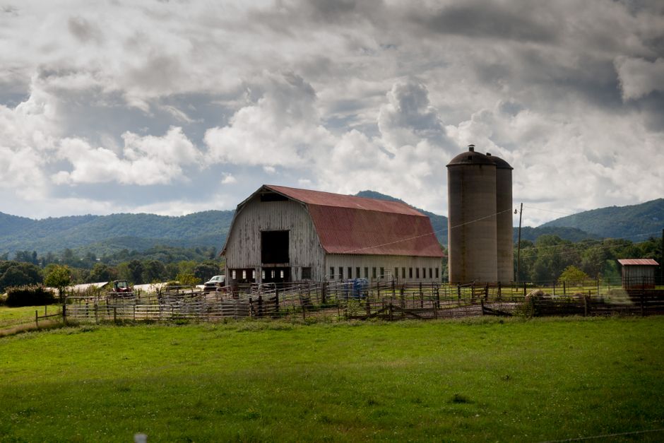 A picturesque barn and silo in Asheville's rural landscape, nestled among rolling hills and lush fields.