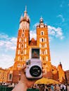 一只手握着宝丽来相机，在克拉科夫主广场拍摄了圣玛丽大教堂，突显了旅行与文化的交融