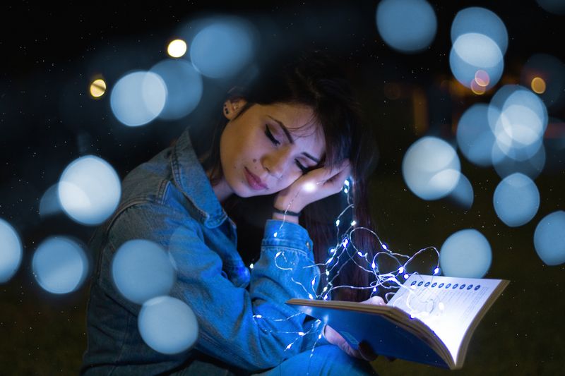 Người phụ nữ thư giãn đọc sách dưới ánh đèn dây lấp lánh ban đêm