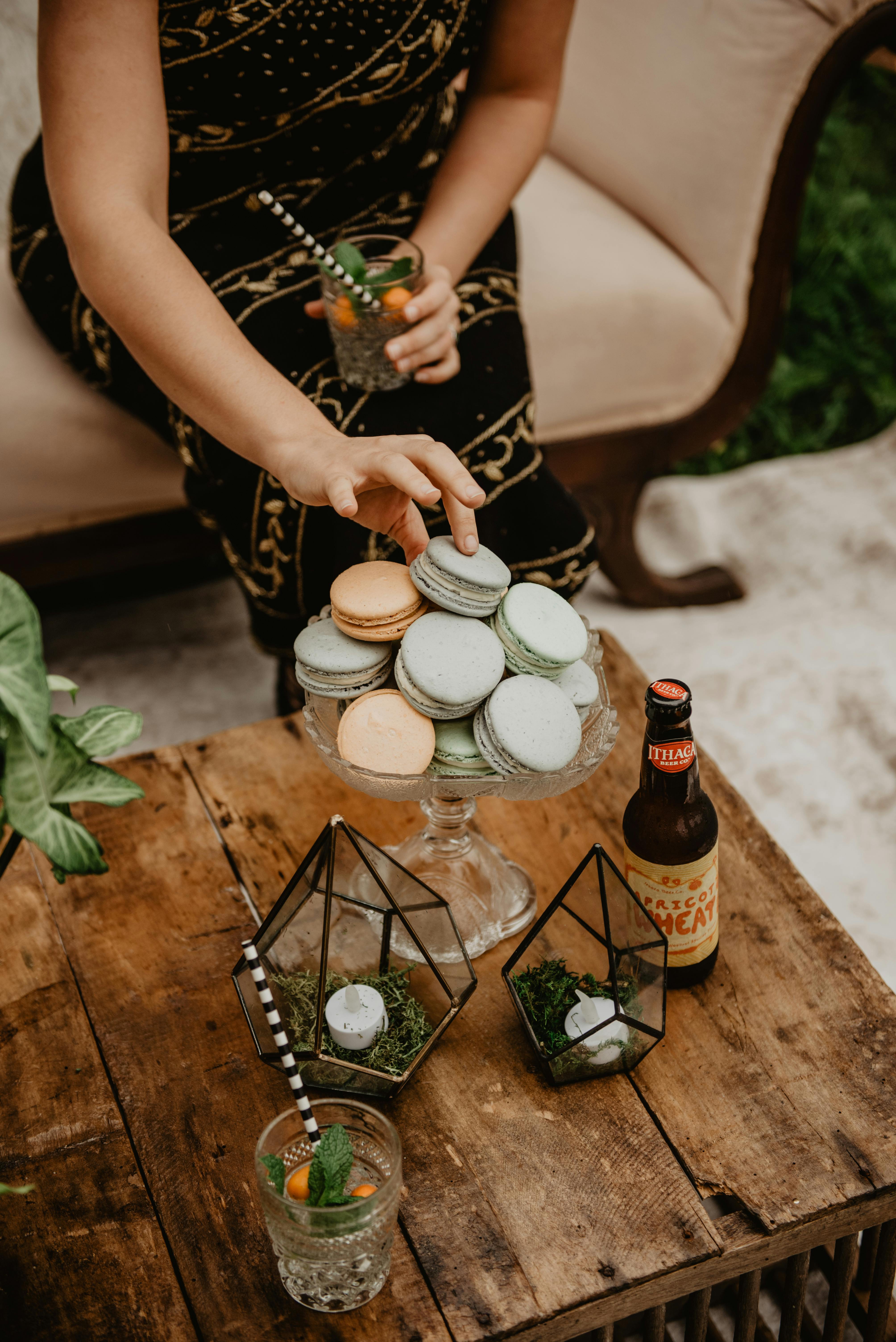 A stylish setup with colorful macarons, an artisan drink, and green decor on a wooden table.