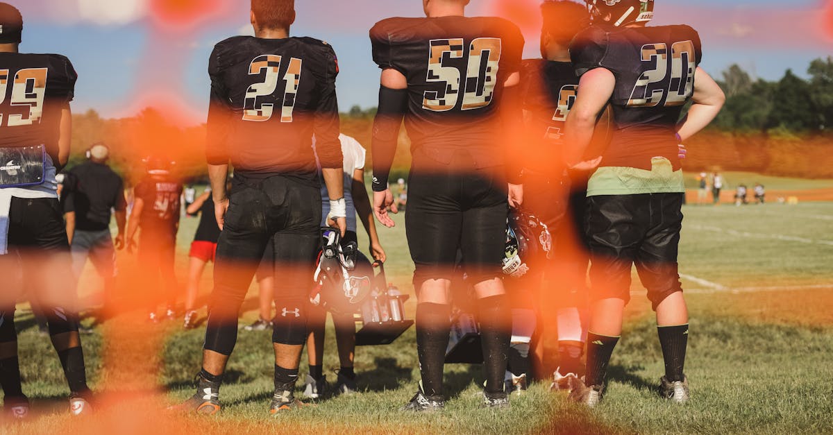 Football players in uniforms on a sunny day, seen from behind through an orange net.