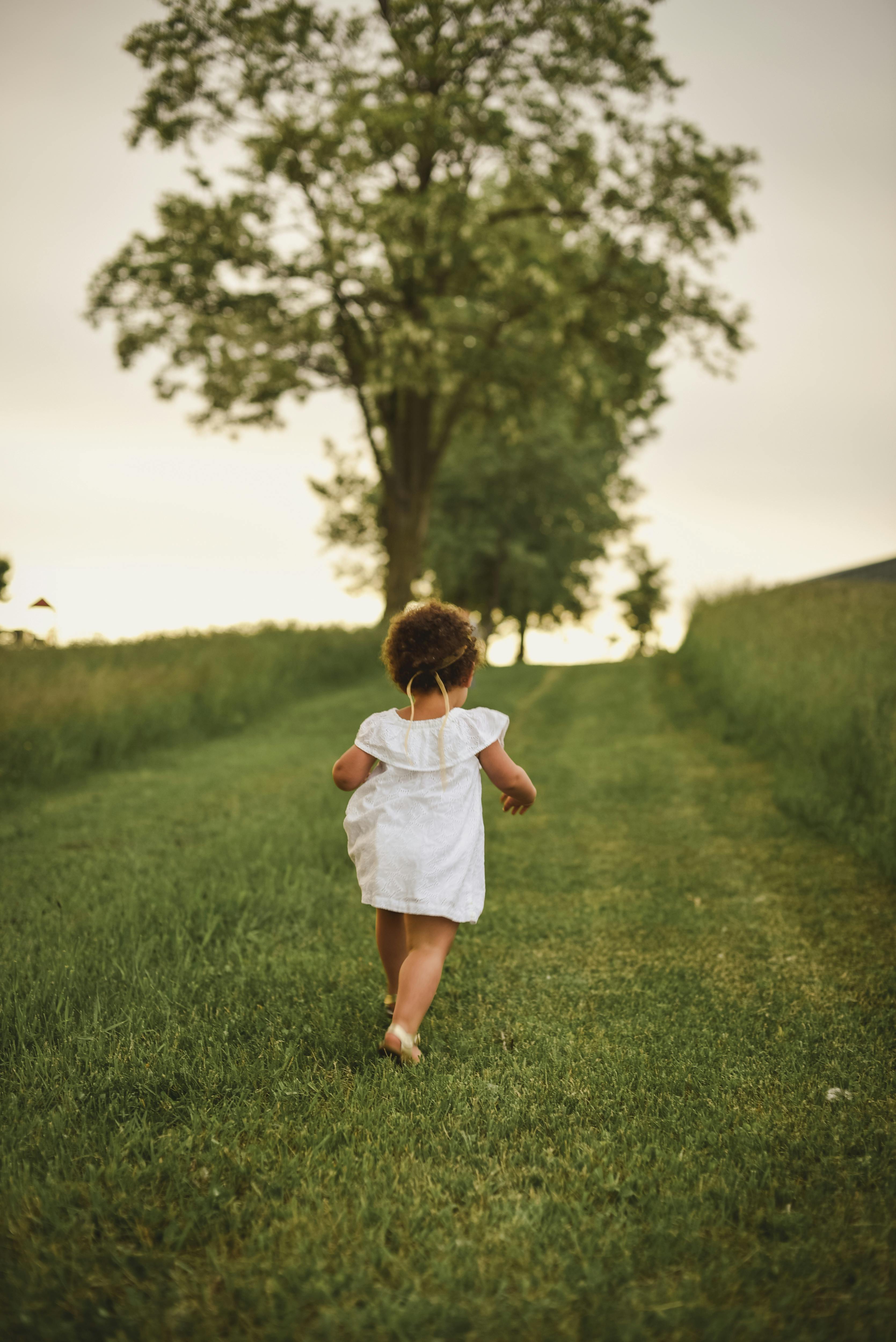 girl standing on grass field facing trees