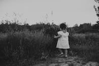 迷人的黑白照片中，一个穿着连衣裙的幼儿在日落时分的草地上探索