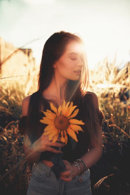 A young woman in a sunlit field holding a sunflower, capturing the essence of summer.