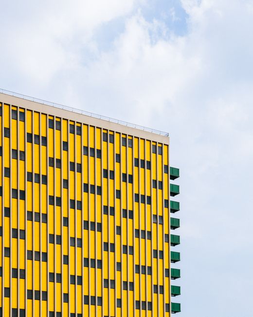 Bright modern building facade with geometric pattern, featuring yellow and green accents under a clear sky.