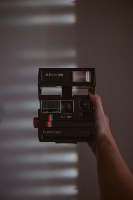 Hand holding a vintage Polaroid camera indoors with dramatic shadow lighting.