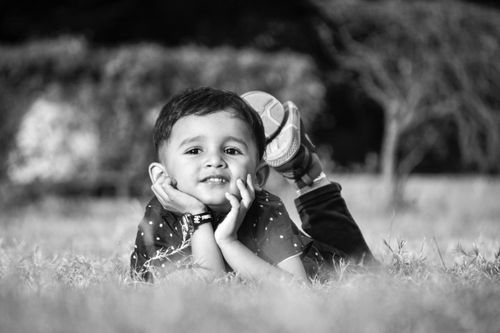 Free Black and white portrait of a happy child lying on grass in a park, enjoying a sunny day. Stock Photo