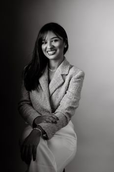 Black and white portrait of a smiling woman in elegant attire, showcasing fashion and poise.